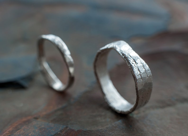May include: Two silver rings with a textured, hammered finish. The rings are lying on a textured, gray surface.