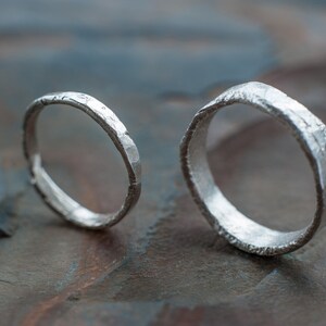 May include: Two silver rings with a hammered texture. The rings are lying on a textured gray surface.