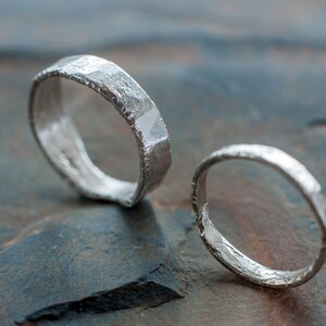 May include: Two silver rings with a textured, hammered finish. The rings are lying on a gray, textured surface.