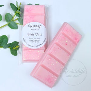 May include: A pink soy wax melt with glitter in a clear plastic wrapper. The wax melt is labelled "Whitcliffe Aromas Fairie Dust 100% Soy Wax Hand Poured in Yorkshire www.whitcliffe aromas.co.uk"