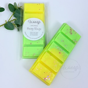 May include: Two wax melts in clear packaging. The wax melts are yellow and green with glitter. The wax melts are labelled "Whitcliffe Aromas Fruity Rings 100% Soy Wax Hand Poured in Yorkshire www.whitcliffearomas.co.uk"