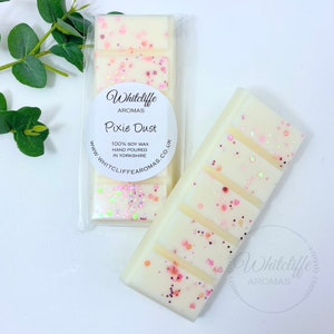 May include: A white soy wax melt with pink glitter and the text "Whitcliffe Aromas Pixie Dust 100% Soy Wax Hand Poured in Yorkshire www.whitcliffe aromas.co.uk"