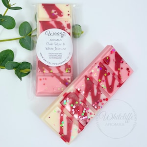 May include: Two pink and white wax melts with a red swirl design and glitter. The wax melts are packaged in clear plastic and have a label that says "Whitcliffe Aromas Pink Tulips & White Jasmine 100% Soy Wax Hand Poured in Yorkshire www.whitcliffe aromas.co.uk"