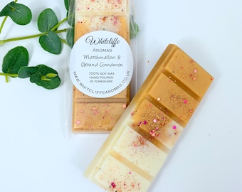 May include: Two wax melts in clear packaging. The wax melts are in a bar shape with four sections. The wax melt on the left is a light brown color with gold glitter. The wax melt on the right is a white and light brown color with gold glitter. The wax melts are labeled "Whitcliffe Aromas Marshmallow & Ground Cinnamon 100% Soy Wax Hand Poured in Yorkshire www.whitcliffearomas.co.uk"