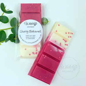 May include: Two wax melts in clear packaging. The wax melts are pink and white with a glittery finish. The packaging has a label that says "Whitcliffe Aromas Cherry Bakewell 100% Soy Wax Hand Poured in Yorkshire www.whitcliffe aromas.co.uk"