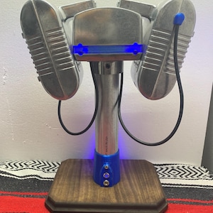 May include: A silver metal sculpture of a robot with blue lights. The robot has two large, round, silver arms and a smaller, round head. The robot is standing on a wooden base.