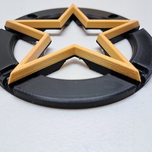 May include: A black circular base with a gold five-pointed star cutout. The star has a raised, layered design.