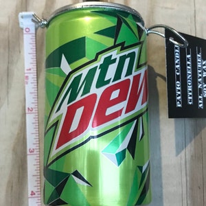 May include: A green and white Mtn Dew can repurposed as a candle holder. The can is approximately 4 inches tall. A black tag with white text hangs from the top, listing "PATIO CANDLE", "CITRONELLA", "ALL NATUREL", and "SOY WAX".