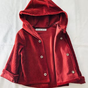 May include: A red corduroy hooded jacket with a button fastening and a label that reads "Encore Gift Collection".