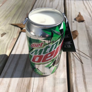 May include: A Diet Mountain Dew can candle with a white wax interior. The can features the Diet Mountain Dew logo in red and green on a silver background. A small tag is attached to the top of the can.