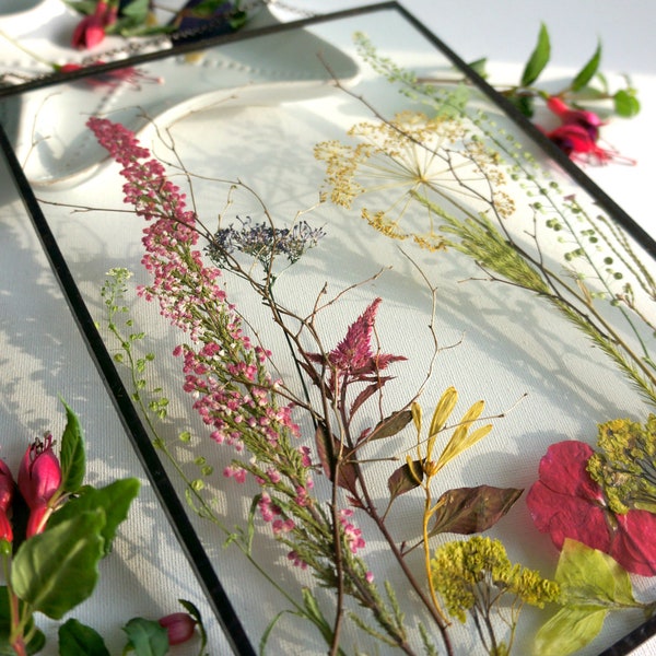 Floral arrangement in glass frame with real pressed flowers. Meadow flowers in  float frame on chain for natural wall decor in eco style