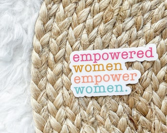 Puede incluir: Dos pegatinas con las palabras «empowered women empower women» en letras rosas, naranjas y turquesas. Las pegatinas están sobre una estera circular tejida, de color canela, con un fondo blanco y esponjoso.