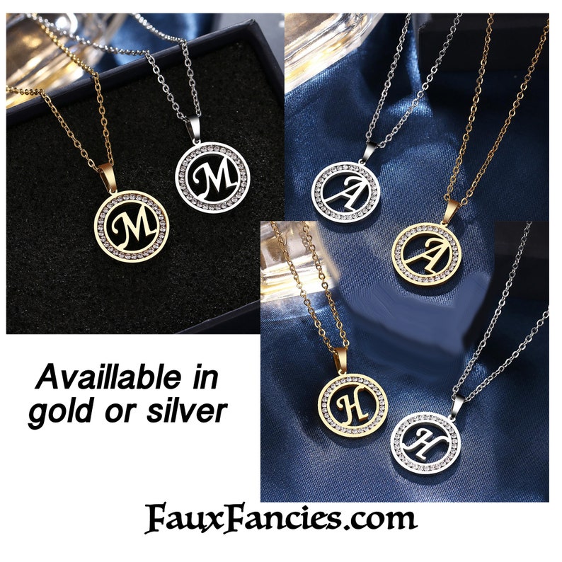 May include: Gold and silver-toned circular pendant necklaces featuring the letters M, A, and H. Each pendant has a central cutout letter surrounded by a ring of small clear crystals on a matching metal chain. Text reads: Available in gold or silver.