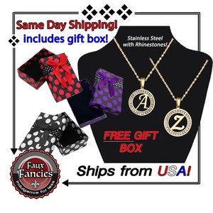 May include: Two gold-tone stainless steel necklaces featuring circular pendants with rhinestones and the letters A and Z. The set includes three patterned gift boxes in red, purple, and white with black polka dots and ribbon bows.