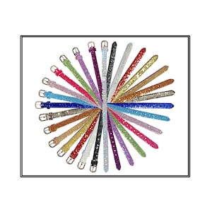 May include: A collection of colorful, sparkly belts arranged in a circular pattern. Each belt is a different color, including red, blue, green, gold, and silver, and is covered in glitter or rhinestones. The belts have gold-colored buckles.