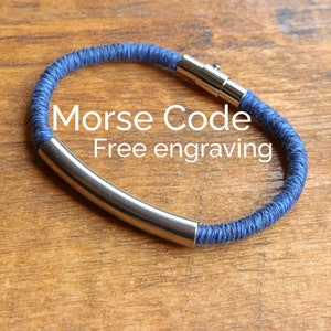 May include: A blue braided bracelet with a silver metal bar. The bracelet has a magnetic clasp. The text "Morse Code Free engraving" is displayed on the image.