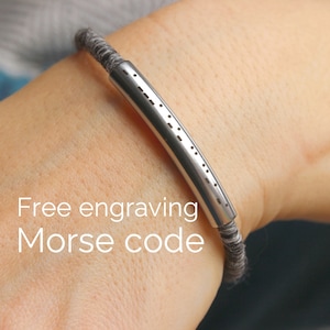 May include: A gray fabric bracelet with a silver bar engraved with Morse code. Free engraving is offered.