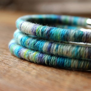 May include: Three stacked bracelets made of woven yarn in shades of blue, green, and white.