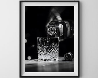 Könnte beinhalten: Schwarzweißfoto einer Hand, die Alkohol aus einer Flasche in ein Kristallglas gießt. Das Glas steht auf einer Holzoberfläche.