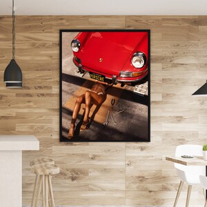 May include: A red vintage Porsche car with a California license plate that reads "PORSCHE" is lifted up on a jack. A person is lying on their back underneath the car, wearing a bikini and high heels.