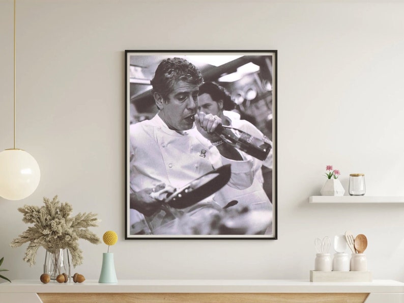 May include: A black and white photograph of a man in a chef's uniform drinking from a bottle while holding a frying pan.