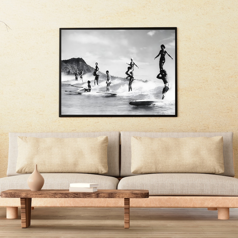 May include: Black and white photograph of a group of people surfing on waves. The photo is framed in a black frame and is hanging on a wall.