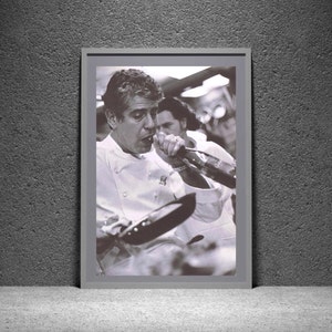 May include: A black and white photograph of a chef wearing a white chef's jacket, drinking from a bottle of wine. The chef is in a kitchen setting and is holding a frying pan in his other hand.