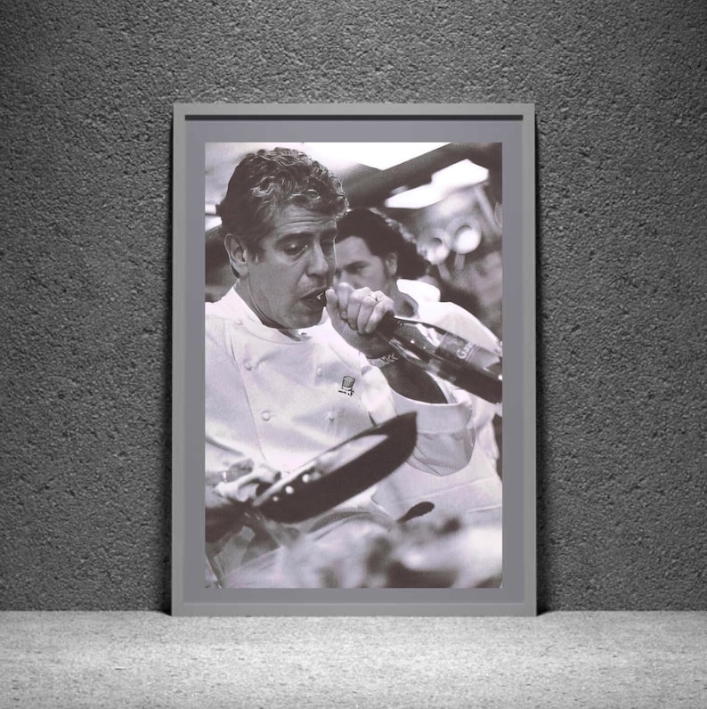 May include: A black and white photograph of a chef wearing a white chef's jacket, drinking from a bottle of wine. The chef is in a kitchen setting and is holding a frying pan in his other hand.