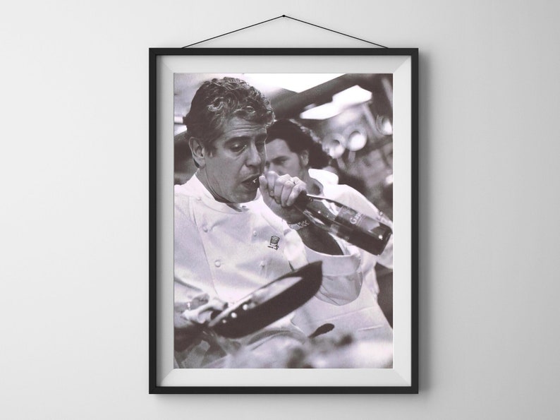 May include: A black and white photograph of a chef wearing a white chef's jacket, drinking from a bottle of wine. The chef is holding a frying pan in his other hand.