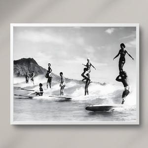 May include: A black and white photograph of a group of people surfing on a beach. The people are standing on surfboards and are riding the waves. The photo is taken from a distance and shows the people in the water.