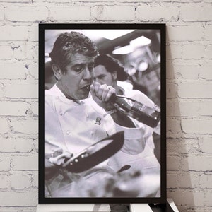 May include: A black and white photograph of a chef wearing a white chef's jacket drinking from a bottle of wine while holding a frying pan.