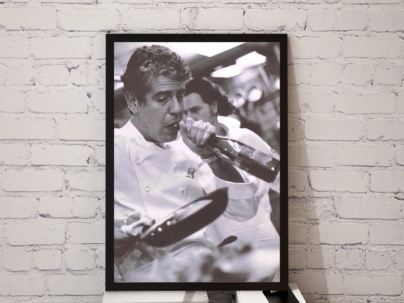 May include: A black and white photograph of a chef wearing a white chef's jacket drinking from a bottle of wine while holding a frying pan.
