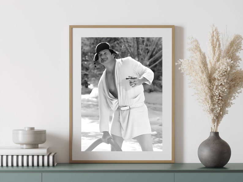 May include: Black and white photograph of a man wearing a white robe and a black fur hat. He is holding a drink in his right hand and smiling at the camera.