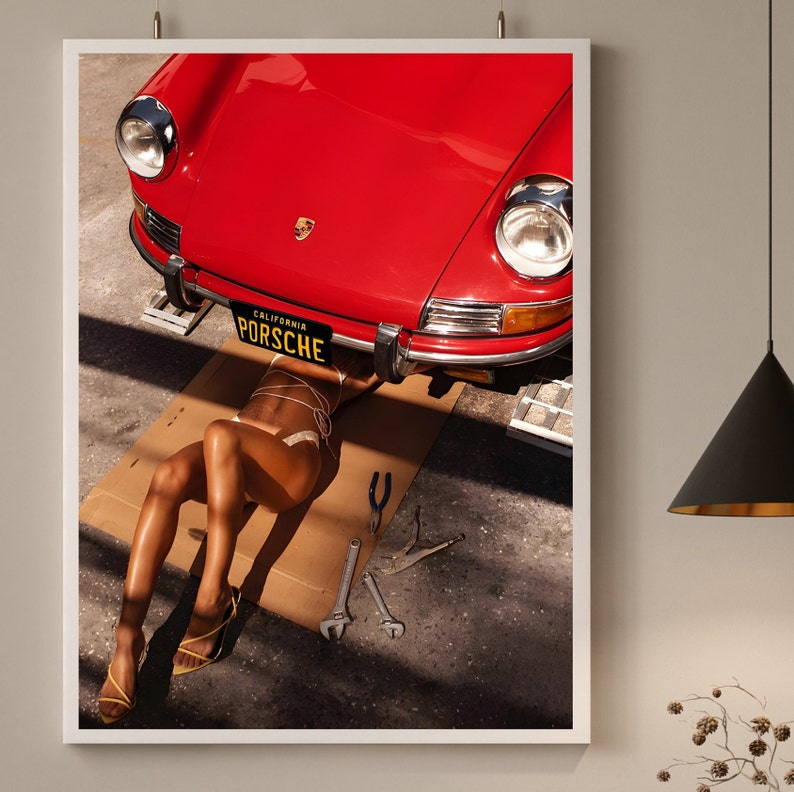 May include: A red vintage Porsche with a California license plate that reads "PORSCHE" is being worked on. A person is lying under the car, wearing a white bikini top and a pair of yellow sandals.