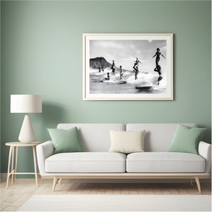 May include: Black and white photograph of a group of people surfing on a beach. The people are standing on surfboards and are in various poses. The beach is in the background and there are mountains in the distance.