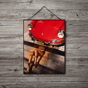 May include: A red vintage Porsche car with a woman lying underneath it. The car has a California license plate that reads "PORSCHE".