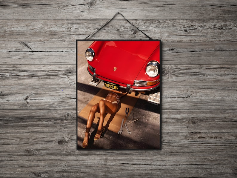 May include: A red vintage Porsche car with a woman lying underneath it. The car has a California license plate that reads "PORSCHE".