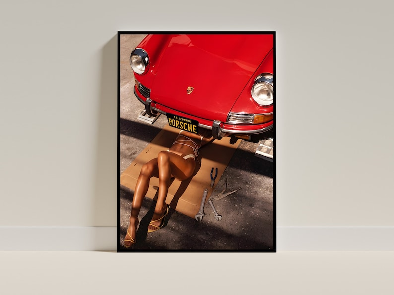May include: A red vintage Porsche car is lifted up on a jack, with a person lying underneath it. The car has a California license plate that reads "PORSCHE".