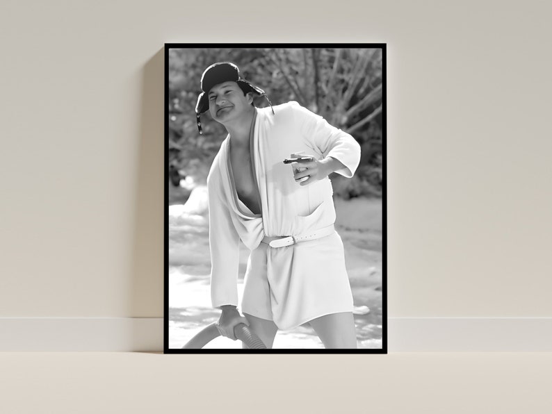 May include: A black and white photo of a person wearing a white robe and a black hat. The person is holding a cigar in one hand and a long object in the other hand. The person is standing in a snowy or icy environment.