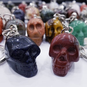 May include: Two skull-shaped keychains made of polished stone. One is dark blue with silver flecks and the other is a deep red. Both have silver key rings.
