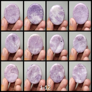 May include: Twelve round, smooth, polished lavender lepidolite stones. Each stone has a unique pattern of white and lavender swirls. The stones are arranged in a grid pattern, with each stone held in a hand.