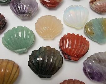 May include: A collection of carved gemstone seashell figurines in various colors, including green, purple, red, and white. The seashells are arranged on a white surface, showcasing their intricate details and natural variations.