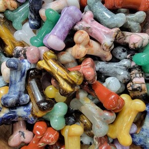 May include: A collection of polished gemstone dog bone shaped charms in various colors, including green, red, purple, blue, brown, and white.