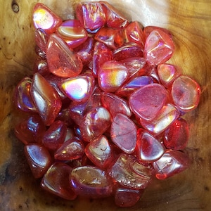 May include: A bowl filled with iridescent red tumbled stones. The stones have a smooth, polished surface and a variety of shapes and sizes.