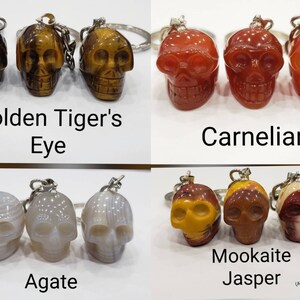 May include: Three sets of three skull-shaped keychains made of different types of stone. The first set is golden tiger's eye, the second is carnelian, and the third is agate. The last set is mookaite jasper. All keychains are discounted due to worn down faces.