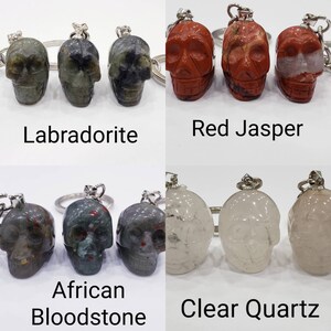 May include: Four sets of skull-shaped keychains made of different types of stones. The stones are Labradorite, Red Jasper, African Bloodstone, and Clear Quartz.
