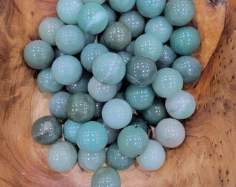 May include: A bowl filled with smooth, green and blue jade spheres. The spheres are various shades of green and blue, with some having a more opaque appearance.