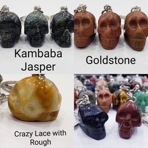 May include: A collection of skull-shaped keychains made from different types of stone. The stones include Kambaba Jasper, Goldstone, Crazy Lace with Rough, and a dark blue stone.