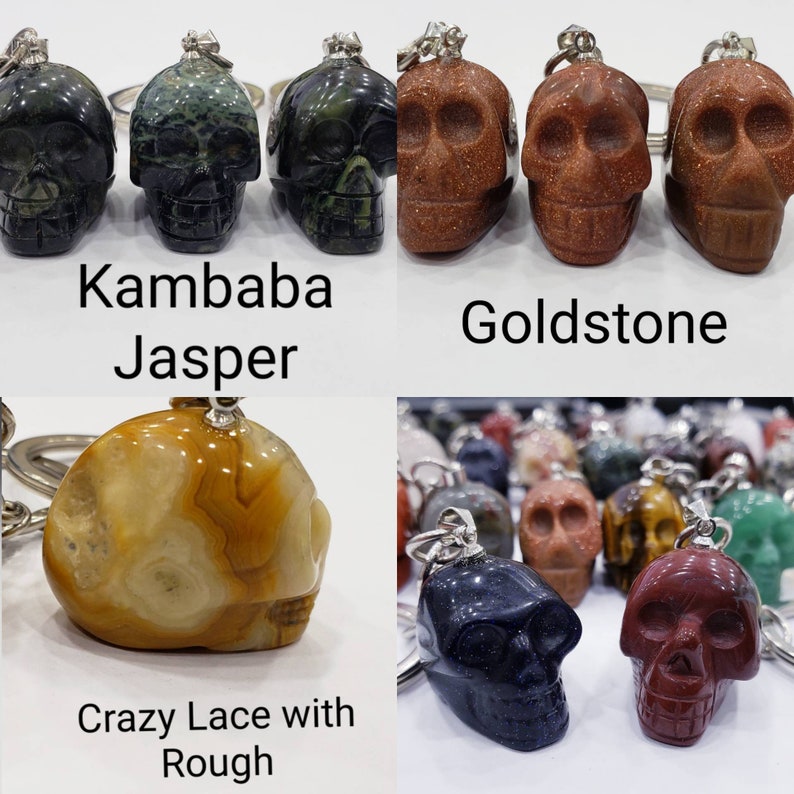 May include: A collection of skull-shaped keychains made from different types of stone. The stones include Kambaba Jasper, Goldstone, Crazy Lace with Rough, and a dark blue stone.