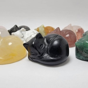 May include: A collection of sleeping cat figurines carved from various types of gemstones, including green, black, white, yellow, and pink.